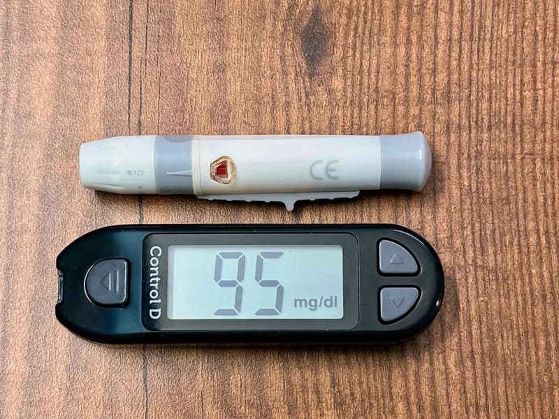Un lecteur de glycémie affichant 95 mg/dl, posé à côté d'un autopiqueur.